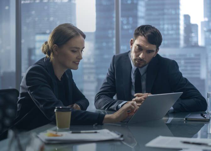 two people sitting at a table looking at a laptop